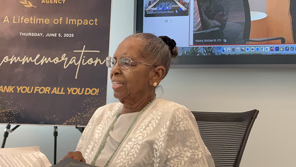 smiling woman sitting next to sign "A Lifetime of Impact"
