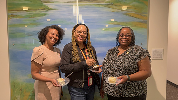 3 women smiling, standing in front of painting
