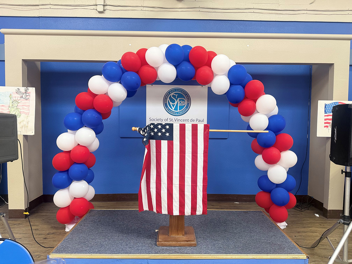 red, white and blue arch in front of American flag and dias